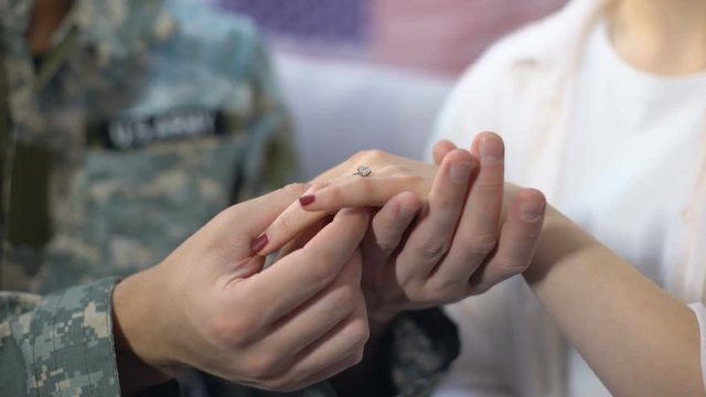 Male soldier putting engagement ring on girlfriends finger, happy marriage