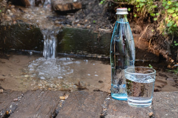 Glass bottle and glass with water on the background of nature. Spring water