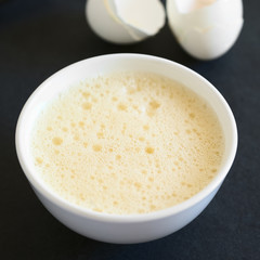 Whisked whole eggs (whites and yolks together) in bowl, with egg shells in the back, photographed on slate with natural light (Selective Focus, Focus in the middle of the whisked egg)
