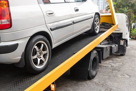 Broken down car towed onto flatbed tow truck with hook cable