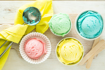Pastel ice cream in white bowls, wood background, copy space
