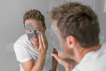 Men beauty caucasian young man applying mud clay detox mask to face. Facial treatment with charcoal...