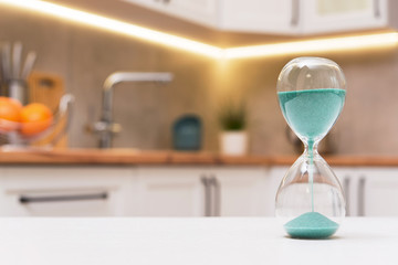 Closeup of hourglass on a white wooden table with defocus kitchen