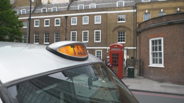Close up view of a taxi sign and a red telephone booth in the background.