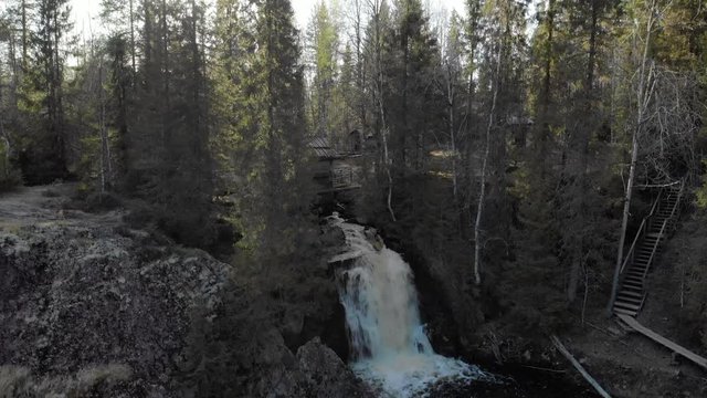 Aerial, rising, drone shot, of the Komulankongas waterfall, in middle oa pine and spruce forest, on a sunny spring day, in Hyyrynsalmi, Kainuu, Finland
