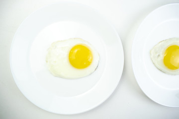 traditional breakfast of two fried eggs. White plate with eggs on the background of a white wooden...