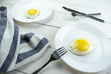 traditional breakfast of two fried eggs. White plate with eggs on the background of a white wooden table. Concept image of breakfast, healthy eating.