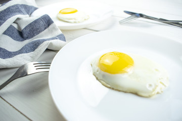 traditional breakfast of two fried eggs. White plate with eggs on the background of a white wooden table. Concept image of breakfast, healthy eating.