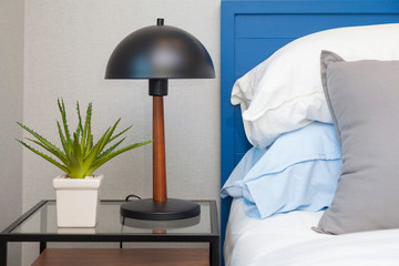 Bed with pillows on the light wall background and a lamp on table.