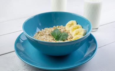 Plate with tasty oatmeal and banana slices on white wood background. Concept image of breakfast, healthy eating.