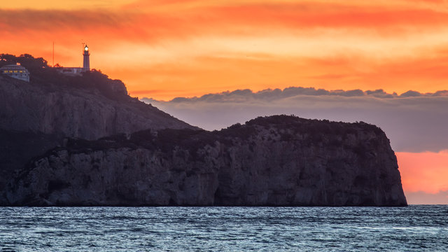 Early morning before sunrise on the Mediterranean sea. On the rocky coast at Cabo de la Nao stands a white lighthouse and in the background the day begins with a dawn.