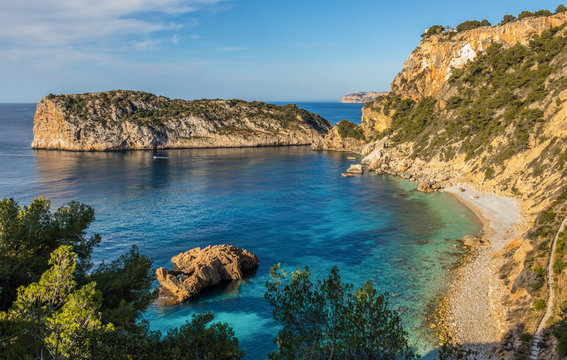 A beautiful rocky bay on the Mediterranean north of the city of Moraira on a sunny day with blue sky and turquoise water.