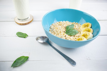 Plate with tasty oatmeal and banana slices on white wood background. Concept image of breakfast, healthy eating.