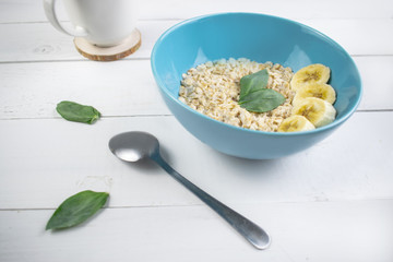 Plate with tasty oatmeal and banana slices on white wood background. Concept image of breakfast, healthy eating.