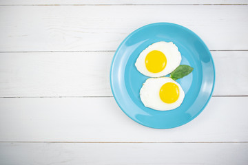 Plate with tasty oatmeal and banana slices and fried eggs on white wood background. Concept image of breakfast, healthy eating.