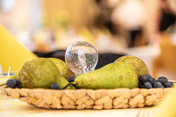 Glühbirne inmitten von echten Birnen und Heidelbeeren in einem Korb
