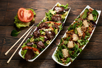Tasty sushi salad served on white plates with chopsticks and tomato on wooden background in restaurant