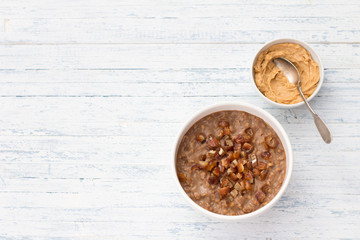 Delicious oatmeal in a white bowl, dates fruits and cocoa. healthy breakfast on light blue background