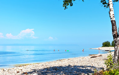 Pebble beach on Lake Baikal. People relax and bathe in the cool water of the lake on a hot summer day. Holiday trips at the weekend. Natural background