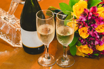 Glasses of champagne and bottle with white label next to wedding bouquet.
