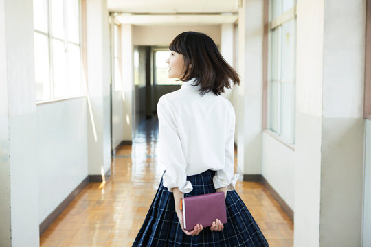 ノートを後ろに持ち廊下を歩く女子高生