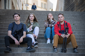 Young traveling people sitting on the stairs. Men holding shooting equipment