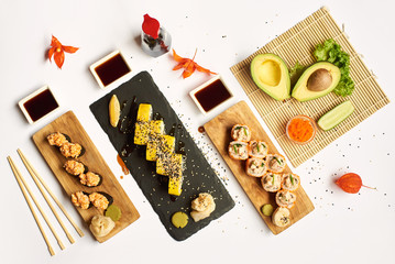 Obraz na płótnie Canvas Different sushi rolls coming with soy sauce, wasabi and marinated ginger from above. Famous Japanese cuisine including meal from rice and seafood. Three different dishes on special offer for lunch.