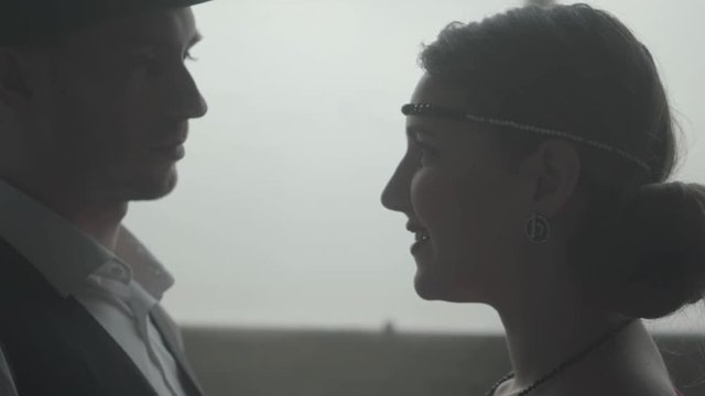 Portrait handsome confident man in a hat whispering joke on the ear of elegant lady, she is laughing. The head of the mafia with his young lovely wife. Criminal authority, cool guys, mafia