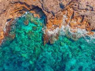 Top view Azure blue sea with waves beating on beach and rocks. Aerial photo.