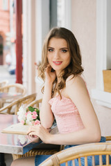 beautiful girl sitting at a table in a cafe. Nearby is a bouquet of pink roses. 