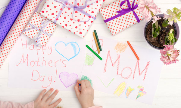 Little girl drawing happy mother's day greeting card with presents on the table. Mothers day background