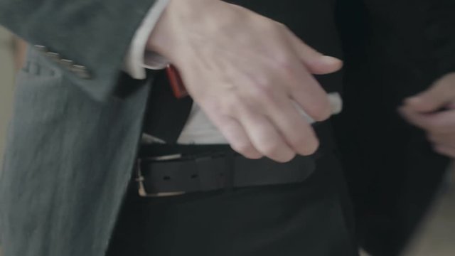 Unrecognizable man in a suit pushes the jacket back and shows the gun hidden behind the belt then covers it again. Criminal authority, mafia, criminal gang, cool guy