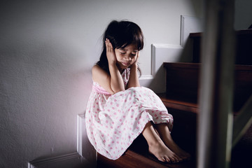 close up a girl who don't want to hear from parents fight, hands cover her ears at the staircase
