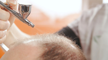Airbrush apply baldness cure over hair close-up