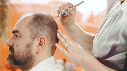 Obraz na płótnie Canvas Hairdresser cure male bald head with spray gun