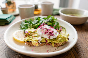 Morning in cafe, oak table. Healthy breakfast with wholemeal bread toast with avocado, poached egg with green salad. Green tea on the Background.