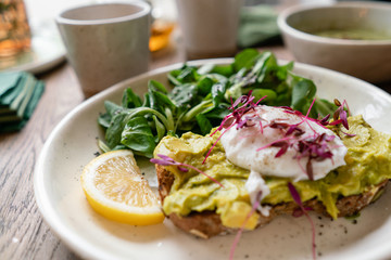 Fototapeta na wymiar Morning in cafe, oak table. Healthy breakfast with wholemeal bread toast with avocado, poached egg with green salad. Green tea on the Background.
