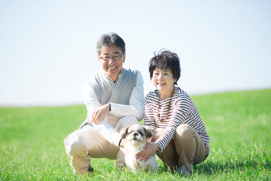 草原で微笑むシニア夫婦と犬