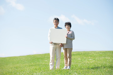 草原でメッセージボードを持つシニア夫婦