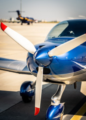Closeup view of white propeller with red endings of the shiny blue sport plane nose