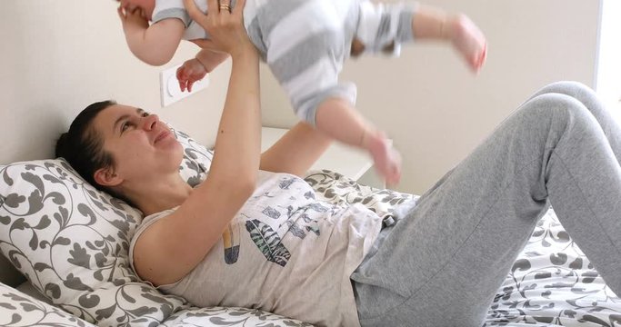 Mother and her baby son having fun and playing at home. Little seven month years old baby play with his mom arms at home at the bed
