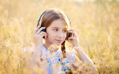 Teenage girl listening to music with headphones in sunshine field