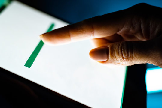 Closeup of tablet with white screen and user's hand on dark background