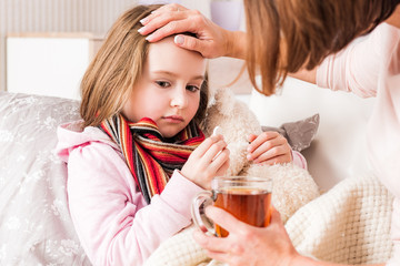 Mum with tea checking little daughter's fever