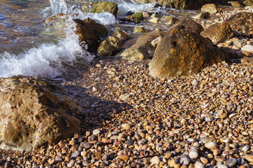 a fragment of a sunny rocky beach with small and large stones and a moving sea wave