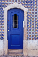 blue wooden door with a metal lattice at the entrance to the house whose walls are covered with ceramic tiles in azulezhu style