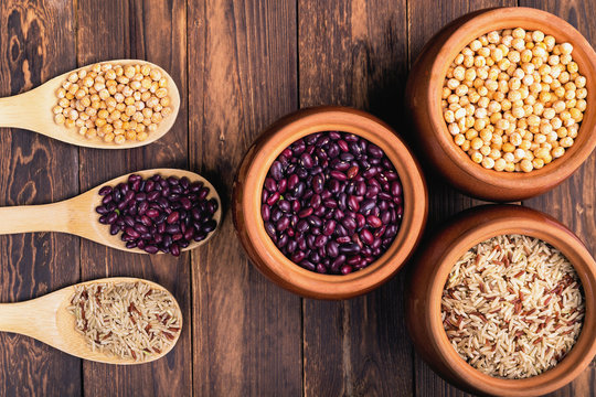three tablespoons and three ceramic pots with beans on a dark wooden background. The concept of natural healthy food