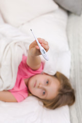 Obraz na płótnie Canvas Sick little child girl lying in bed with thermometer. child shows a thermometer with high temperature