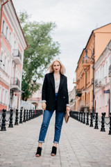 Outdoor portrait of beautiful young woman with blonde hair. Stylish girl in a black jacket and blue jeans posing on the street. Fashion model