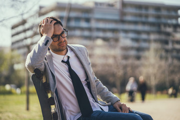 Young businessman is very tired. He is relaxing in park. 